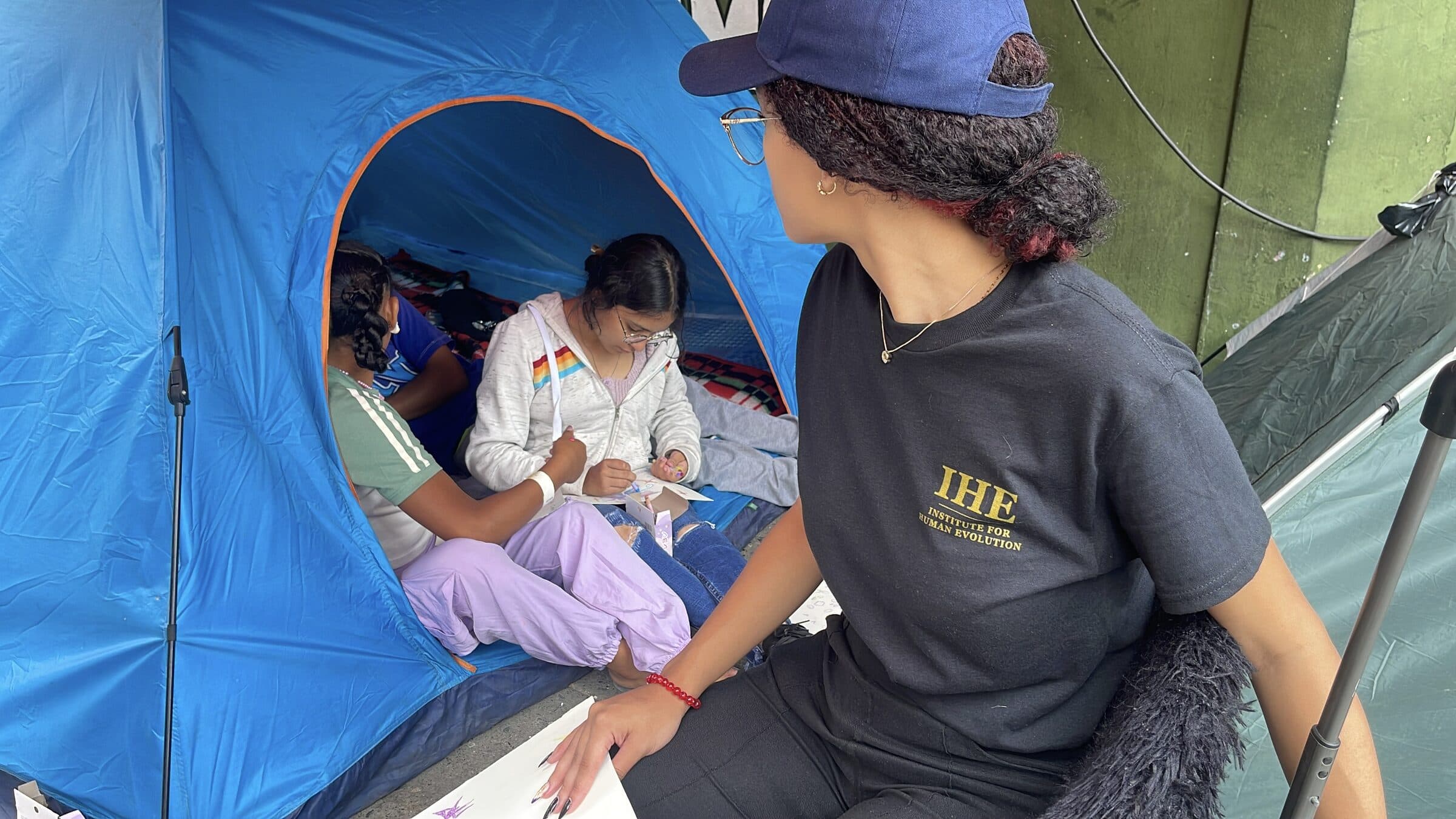 A teenager draws inside a tent beside an IHE volunteer during a quiet moment of the art workshop.