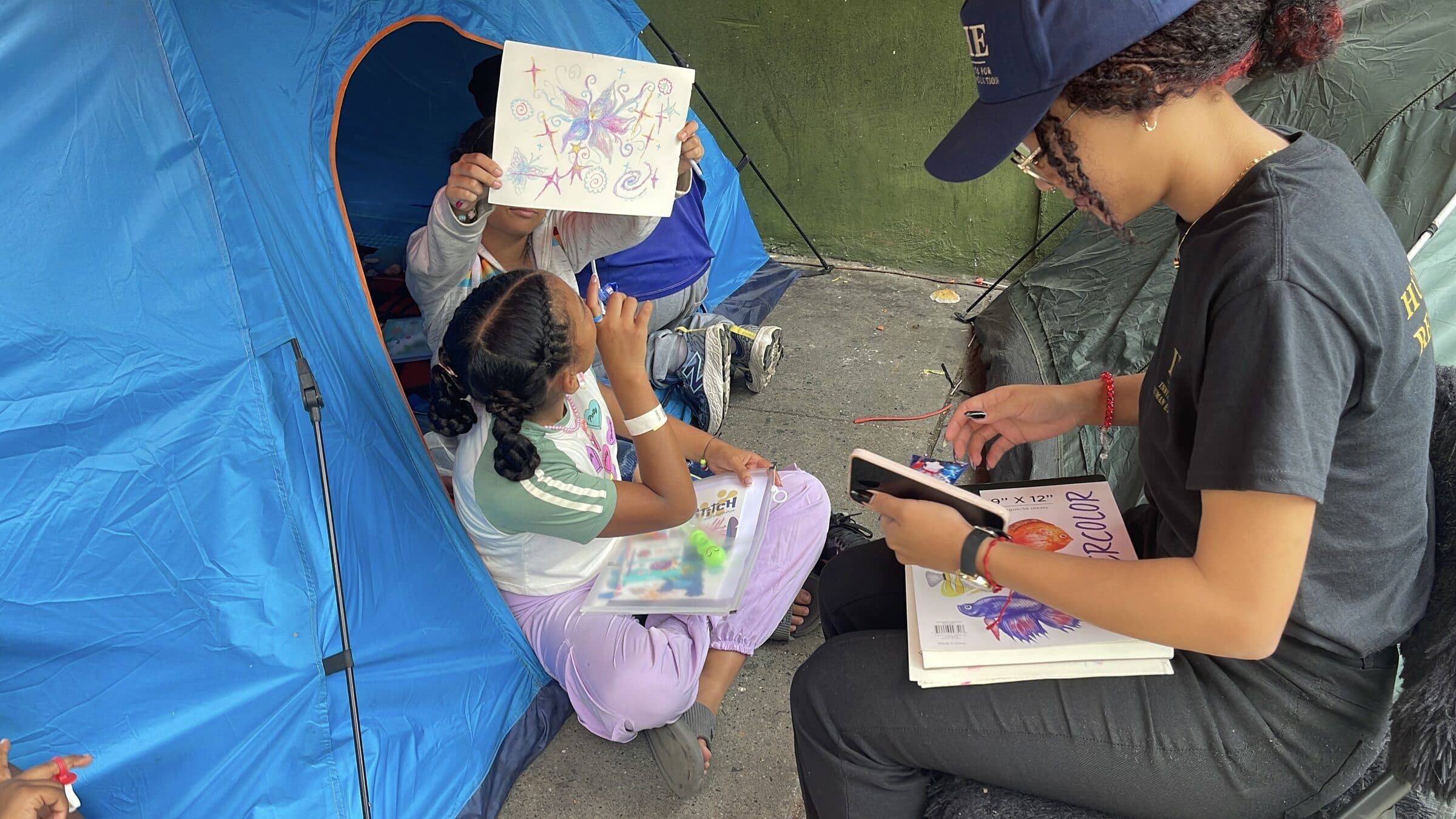 A girl proudly holds up her butterfly drawing, the paper covering her face, during an art workshop at the camp.