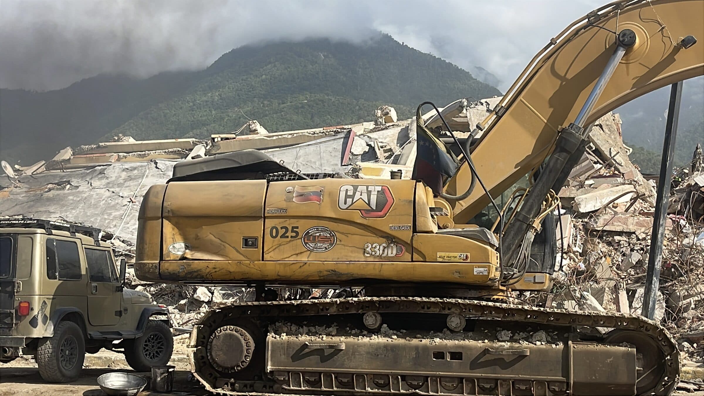 CAT excavator flying a Venezuelan flag during debris removal at collapsed buildings in La Guaira.