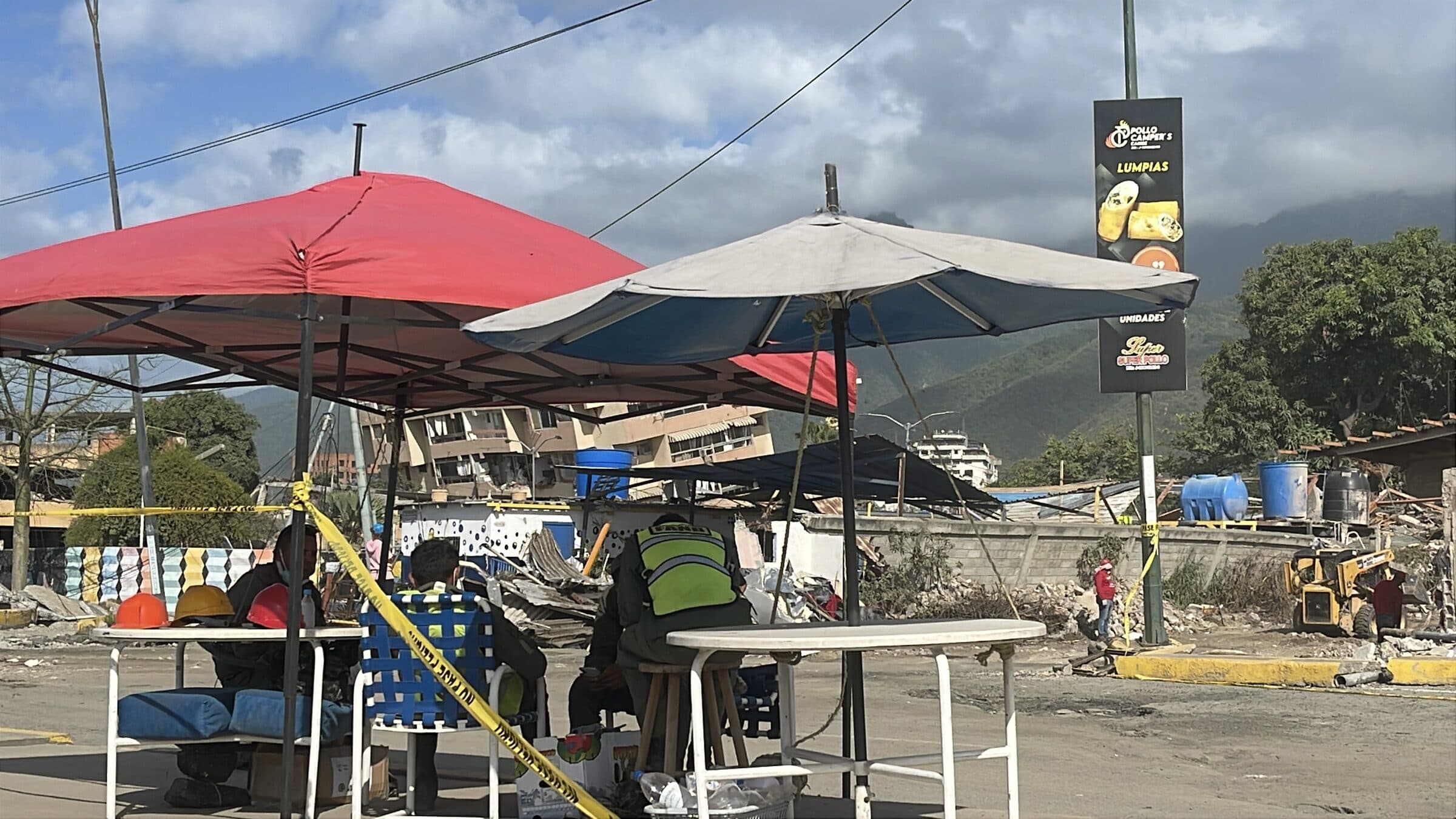 Rescue and military personnel at a field coordination point under umbrellas near the earthquake zone in La Guaira.