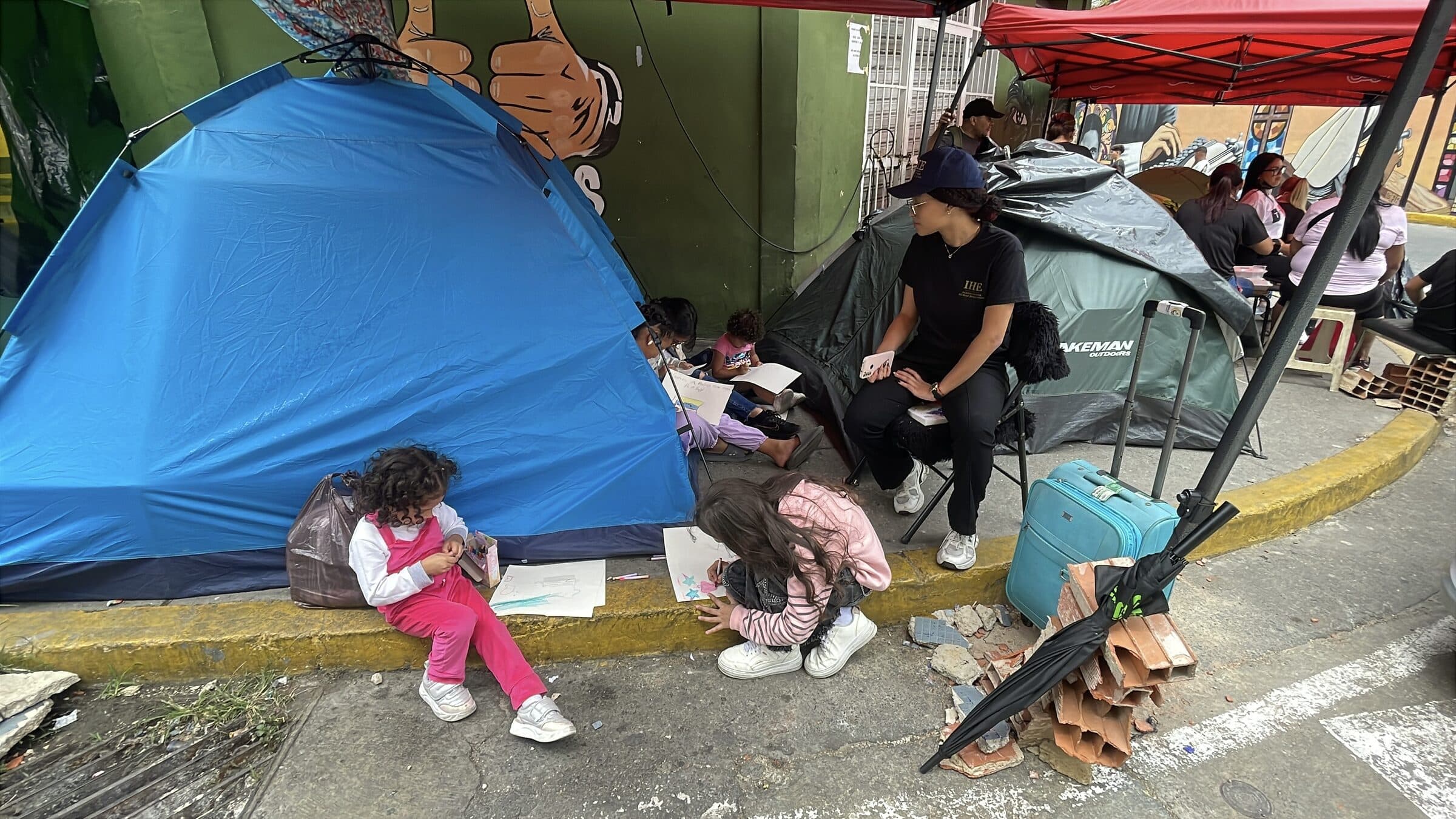 Children draw with crayons on the sidewalk beside tents at the Ojitos de Chávez camp during an IHE art workshop.