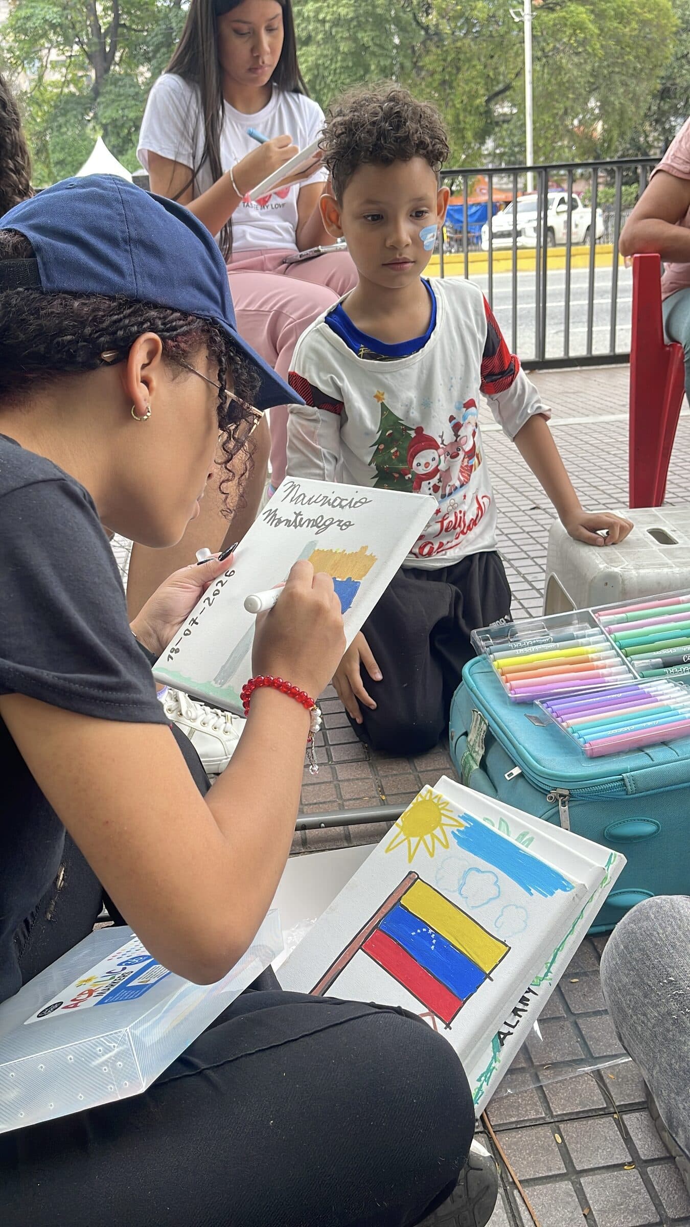 An IHE volunteer signs a finished canvas while the young artist watches closely.