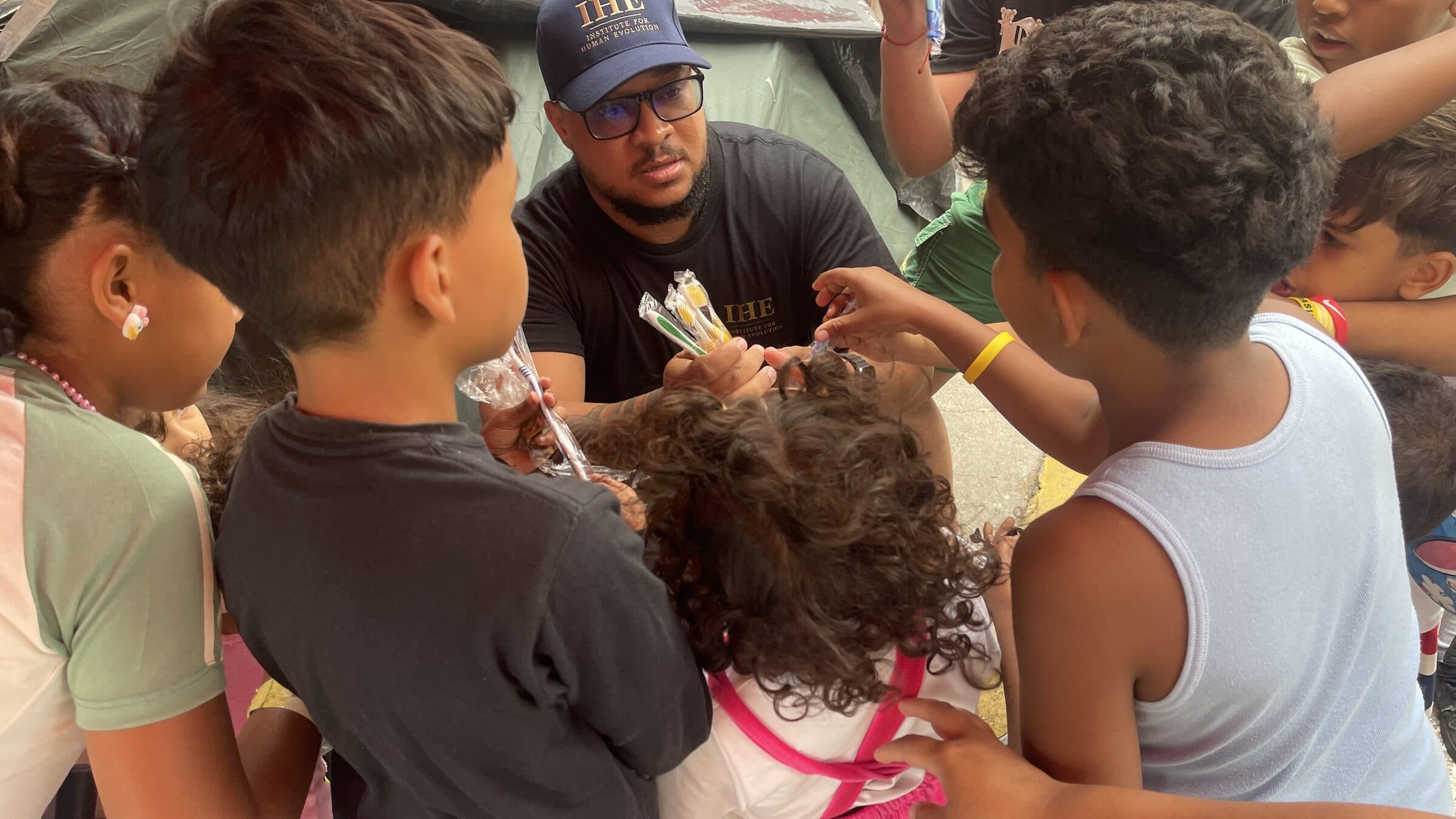 A member of the IHE team hands toothbrushes to children who reach out to receive them at the camp.